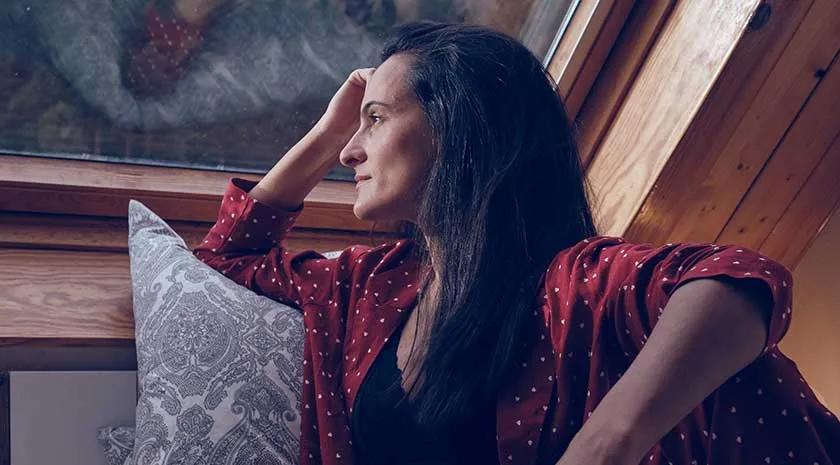 A thoughtful woman looking out of a bedroom window
